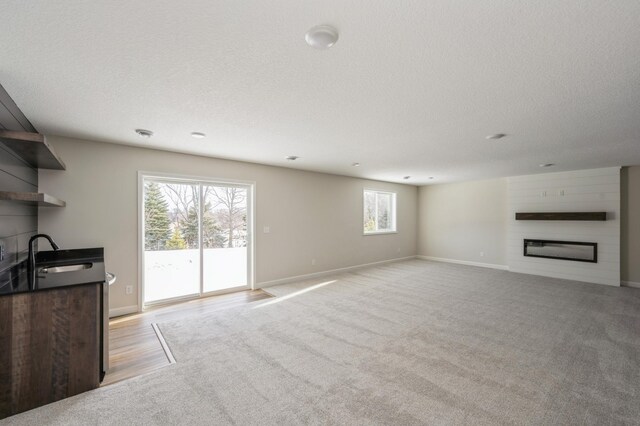 869 Greywood Blvd SW, Delano, MN 55328 - unfurnished living room with a sink, a large fireplace, light colored carpet, baseboards, and a textured ceiling