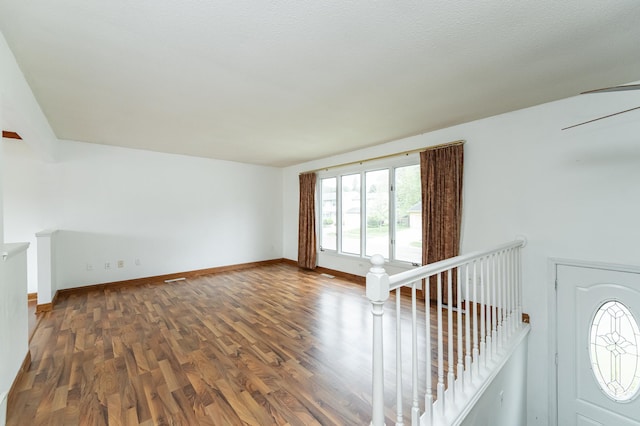 unfurnished living room featuring healthy amount of natural light, dark wood-style flooring, and baseboards