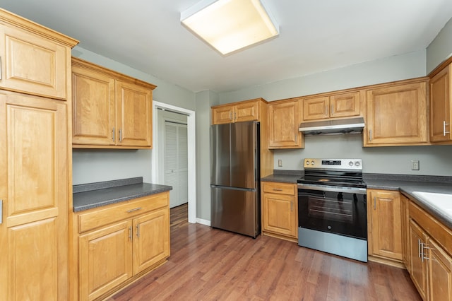 kitchen featuring stainless steel appliances, under cabinet range hood, dark countertops, wood finished floors, and baseboards