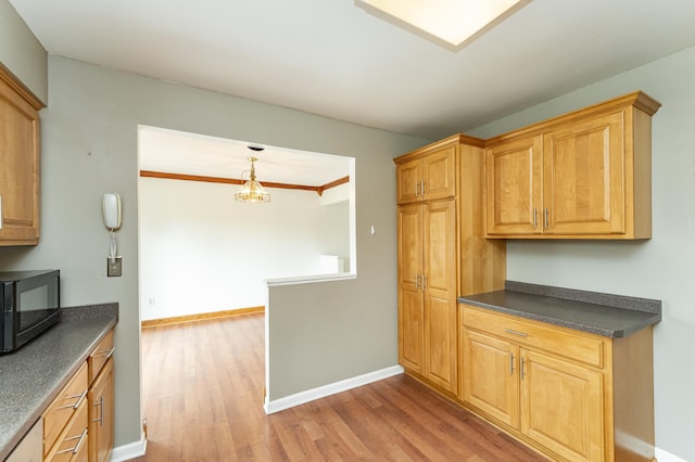 kitchen featuring black microwave, dark countertops, light wood finished floors, baseboards, and pendant lighting