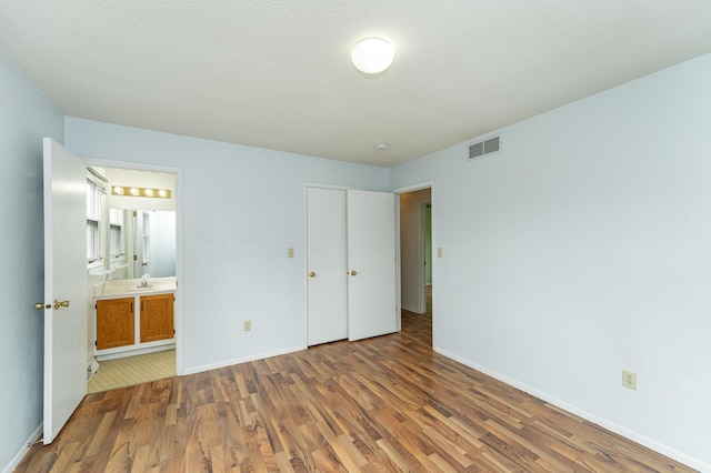unfurnished bedroom with wood finished floors, baseboards, and connected bathroom