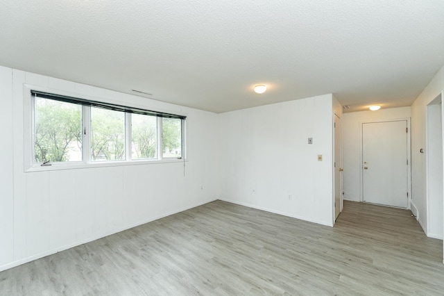 spare room with light wood-type flooring, a textured ceiling, and baseboards
