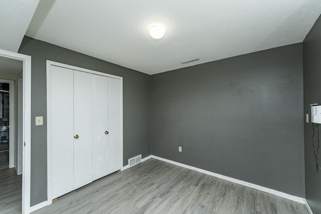 unfurnished bedroom featuring wood finished floors, a closet, baseboards, and a textured ceiling