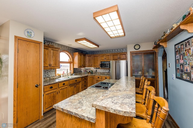 28040 Anchor Rd, Detroit Twp, MN 56501 - kitchen featuring appliances with stainless steel finishes, a sink, wood finished floors, a kitchen island, and brown cabinetry