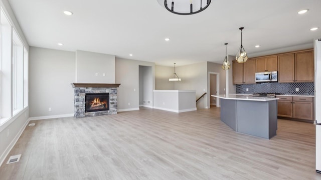kitchen with appliances with stainless steel finishes, light countertops, a center island, tasteful backsplash, and brown cabinets