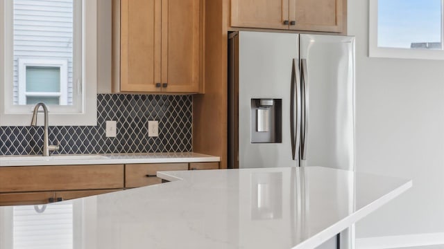 kitchen with stainless steel fridge, a sink, decorative backsplash, and brown cabinetry