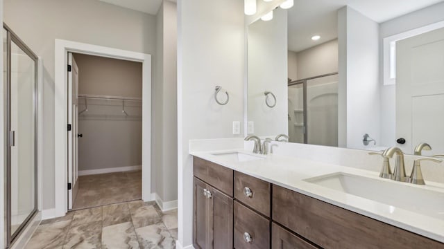 full bath with a shower stall, a walk in closet, marble finish flooring, double vanity, and baseboards