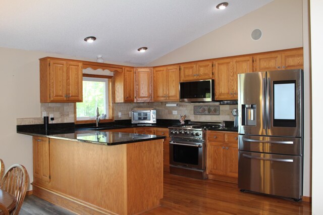 1803 214th Ave NE, East Bethel, MN 55011 - kitchen featuring stainless steel appliances, lofted ceiling, a peninsula, wood finished floors, and decorative backsplash