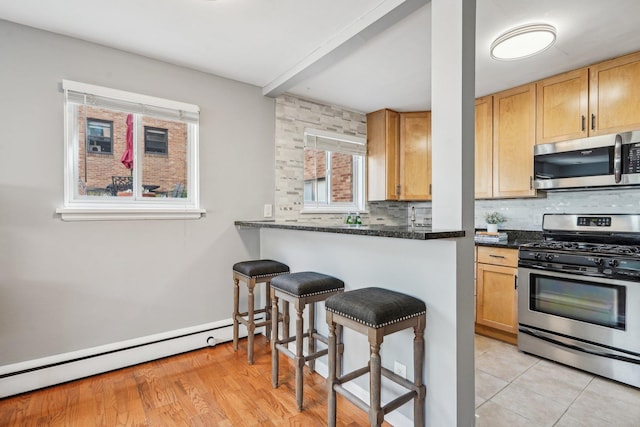 4515 Grand Ave S Unit 1, Minneapolis, MN 55419 - kitchen with appliances with stainless steel finishes, a kitchen breakfast bar, a baseboard heating unit, and decorative backsplash