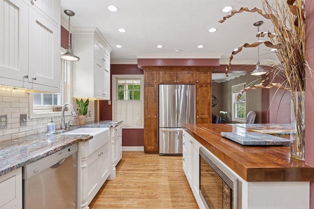 kitchen featuring appliances with stainless steel finishes, crown molding, butcher block countertops, plenty of natural light, and a sink