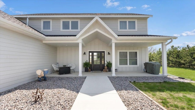 view of exterior entry featuring board and batten siding, a porch, a shingled roof, and central air condition unit