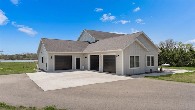 view of front of home with board and batten siding, an attached garage, driveway, a front yard, and a water view