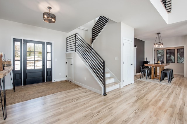 foyer entrance featuring light wood finished floors, a chandelier, stairway, and baseboards