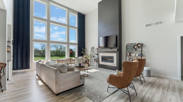 living area featuring a towering ceiling, a glass covered fireplace, wood finished floors, and baseboards