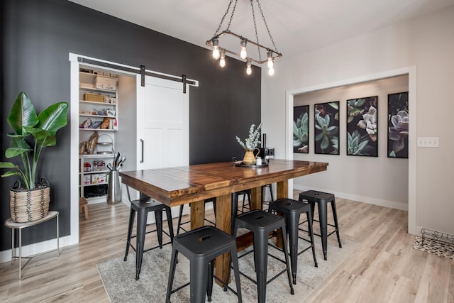 dining area featuring a barn door, light wood-style flooring, and baseboards