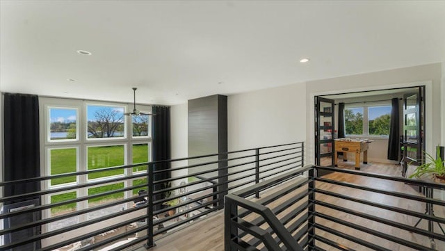 hallway featuring light wood-style floors, an upstairs landing, recessed lighting, and a water view