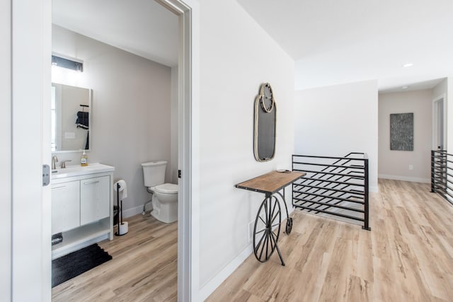 hallway featuring light wood-style flooring, baseboards, an upstairs landing, and a sink