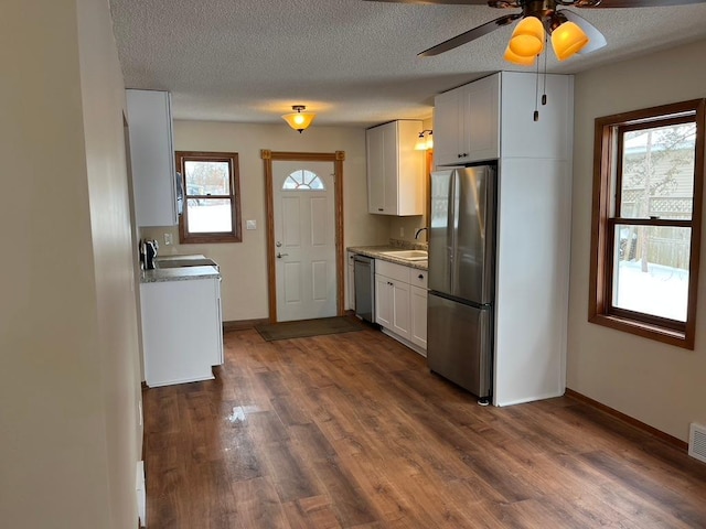 kitchen featuring stainless steel appliances, a sink, dark wood-type flooring, baseboards, and a textured ceiling