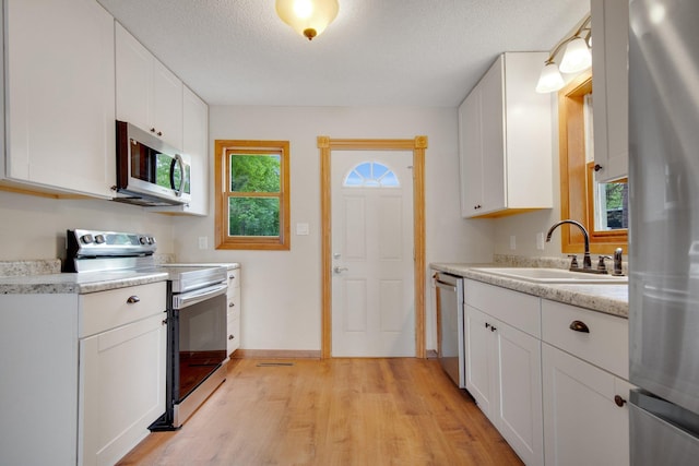 22718 Martin Lake Dr NE, Linwood Twp, MN 55092 - kitchen featuring stainless steel appliances, light wood-style flooring, light countertops, white cabinetry, and a textured ceiling