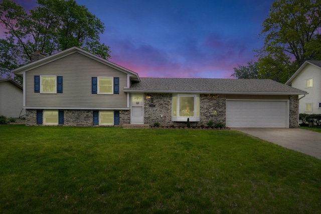 tri-level home featuring a garage, a yard, driveway, a shingled roof, and a chimney