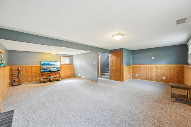 unfurnished living room featuring wooden walls, a wainscoted wall, stairway, and carpet