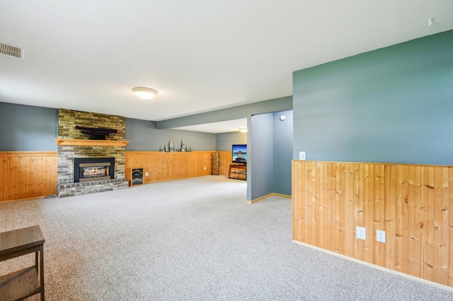 unfurnished living room featuring wooden walls, a wainscoted wall, carpet, and a brick fireplace