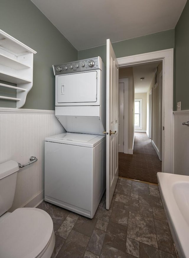 711 2nd St W, Northfield, MN 55057 - bathroom with stacked washer / drying machine, toilet, a wainscoted wall, and stone finish floors
