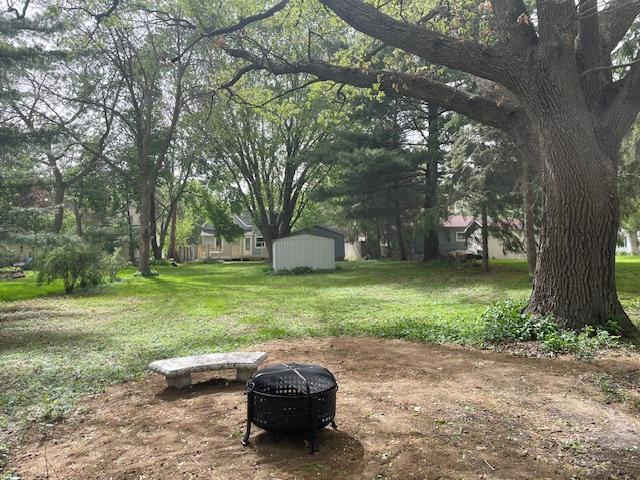 view of green lawn with a fire pit, a shed, and an outbuilding