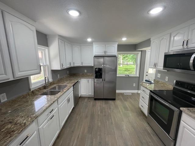 kitchen with stainless steel appliances, a sink, white cabinetry, light stone countertops, and recessed lighting