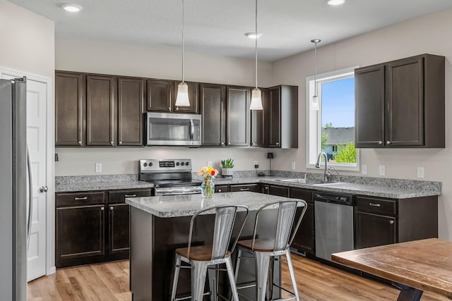 kitchen with stainless steel appliances, a sink, light wood-style floors, dark brown cabinetry, and a kitchen bar