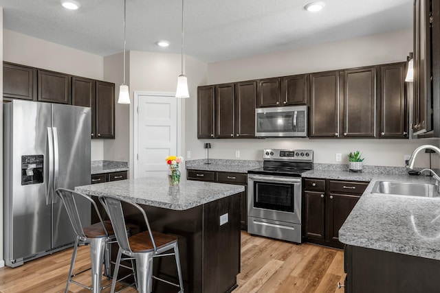kitchen featuring appliances with stainless steel finishes, a sink, dark brown cabinetry, a kitchen island, and light wood finished floors