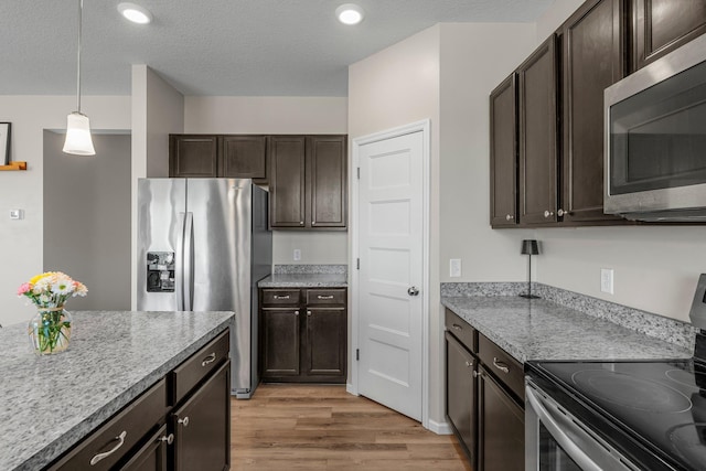 kitchen featuring stainless steel appliances, dark brown cabinetry, light wood-type flooring, decorative light fixtures, and a textured ceiling