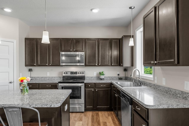kitchen with appliances with stainless steel finishes, a sink, dark brown cabinets, and light wood-style floors