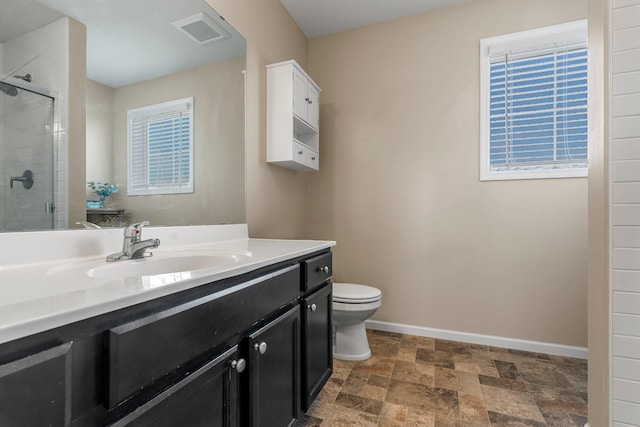 bathroom featuring a stall shower, toilet, vanity, stone finish flooring, and baseboards