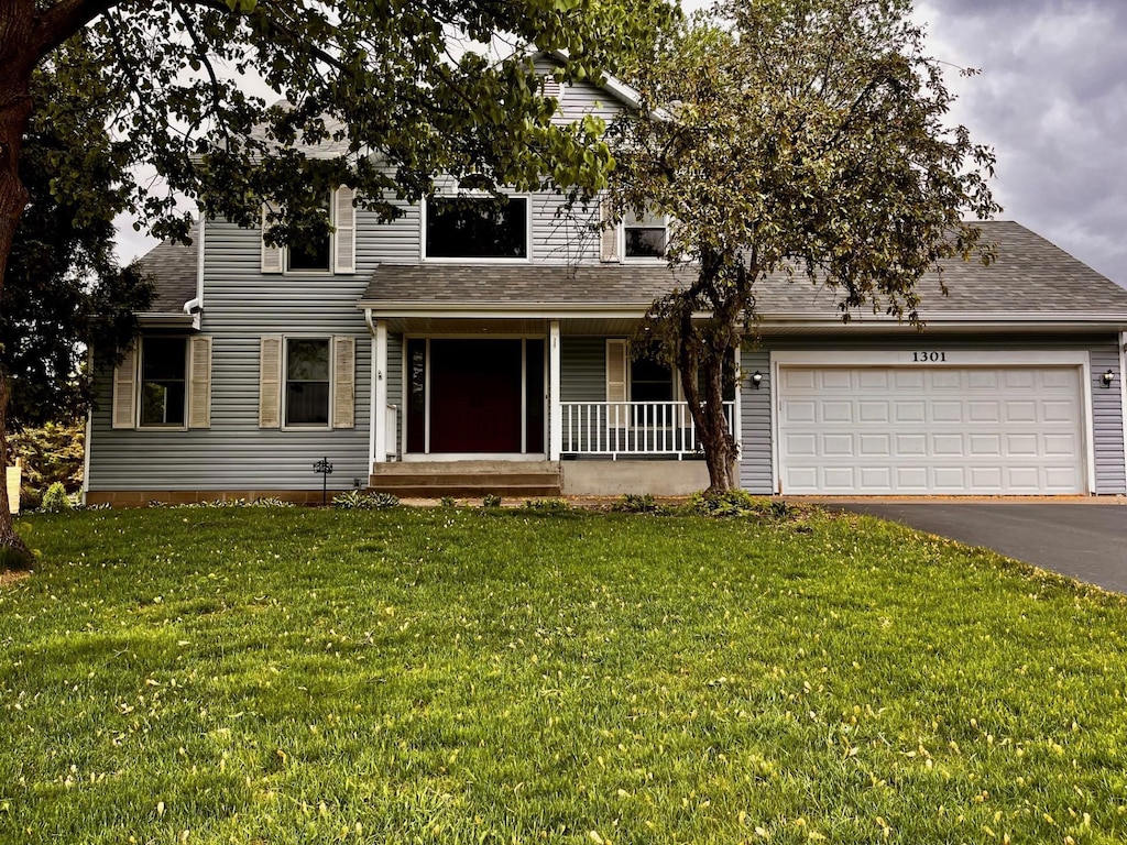 view of front facade featuring covered porch, asphalt driveway, a shingled roof, a front yard, and a garage