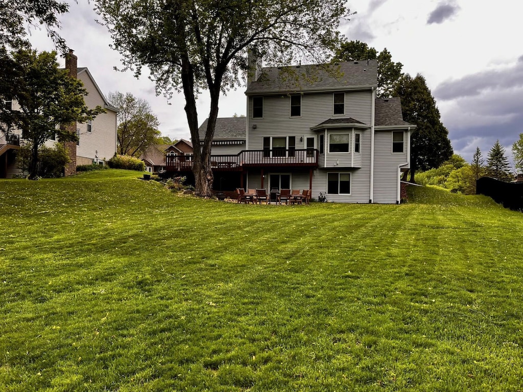 rear view of property with a deck, a lawn, and a patio