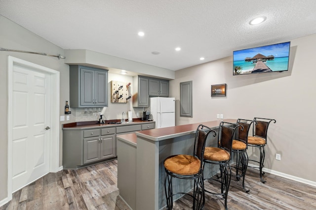 18764 Farmstead Cir, Eden Prairie, MN 55347 - kitchen with freestanding refrigerator, gray cabinets, a kitchen breakfast bar, light wood-style flooring, and a textured ceiling