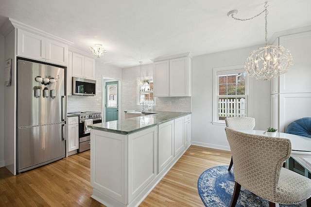 kitchen featuring stainless steel appliances, a chandelier, light wood-type flooring, and tasteful backsplash