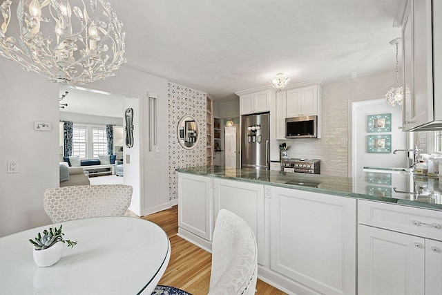 kitchen with stainless steel appliances, light wood-type flooring, white cabinetry, a peninsula, and a chandelier