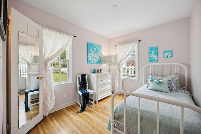 bedroom with multiple windows, light wood finished floors, and baseboards