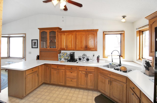 kitchen with a sink, a peninsula, a ceiling fan, light countertops, and brown cabinetry
