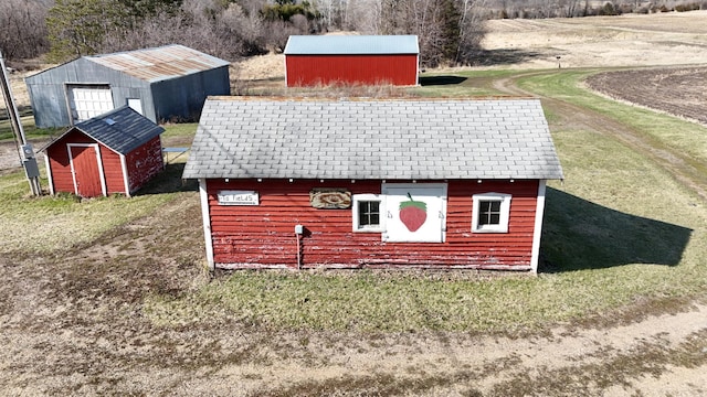 view of side of property featuring an outbuilding, a storage shed, a yard, and a shingled roof