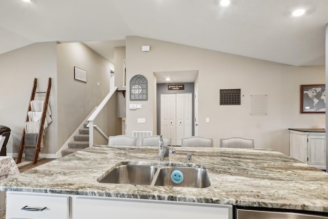 7516 Ochoa Ave NE, Otsego, MN 55330 - kitchen with lofted ceiling, a sink, light stone counters, a center island with sink, and white cabinetry
