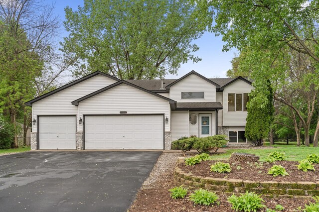 15110 Ute St NW, Ramsey, MN 55303 - tri-level home with driveway, an attached garage, a shingled roof, and brick siding