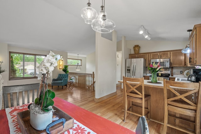 15110 Ute St NW, Ramsey, MN 55303 - kitchen with appliances with stainless steel finishes, lofted ceiling, light wood finished floors, brown cabinetry, and tasteful backsplash