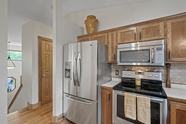 15110 Ute St NW, Ramsey, MN 55303 - kitchen featuring stainless steel appliances, brown cabinetry, light countertops, light wood-style floors, and decorative backsplash