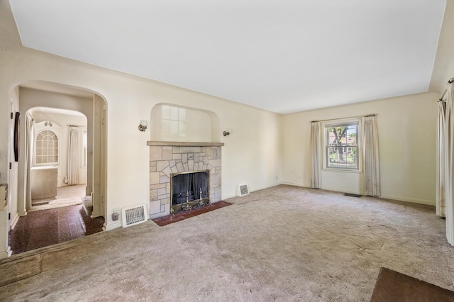 unfurnished living room with carpet floors, a stone fireplace, baseboards, and arched walkways