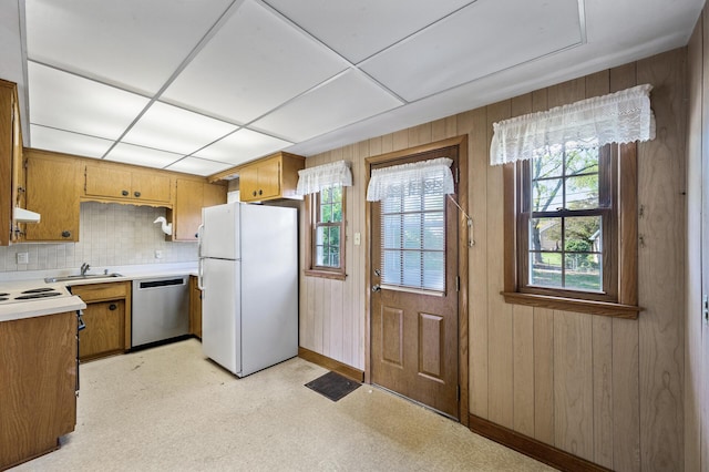 kitchen with freestanding refrigerator, stainless steel dishwasher, a sink, plenty of natural light, and wooden walls