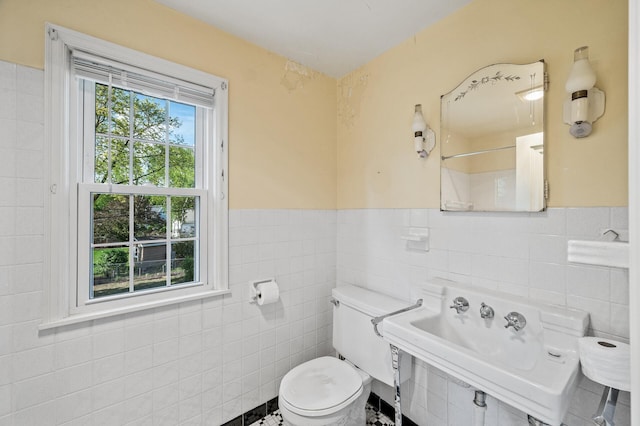 bathroom featuring tile walls, toilet, a wainscoted wall, and a sink