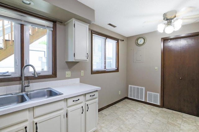 kitchen featuring a sink, a ceiling fan, light countertops, white cabinetry, and baseboards